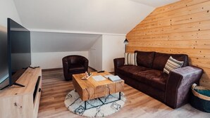 A modern living room with a wooden ceiling, a brown leather sofa, a wooden coffee table, and a flat-screen TV. - L'Ecureuil apartment, Finnish bath on the edge of the forest. Pets allowed (Gérardmer)