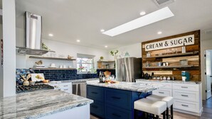 Een moderne keuken met een centraal eiland, inbouwapparatuur en een 'Cream & Sugar' bord.