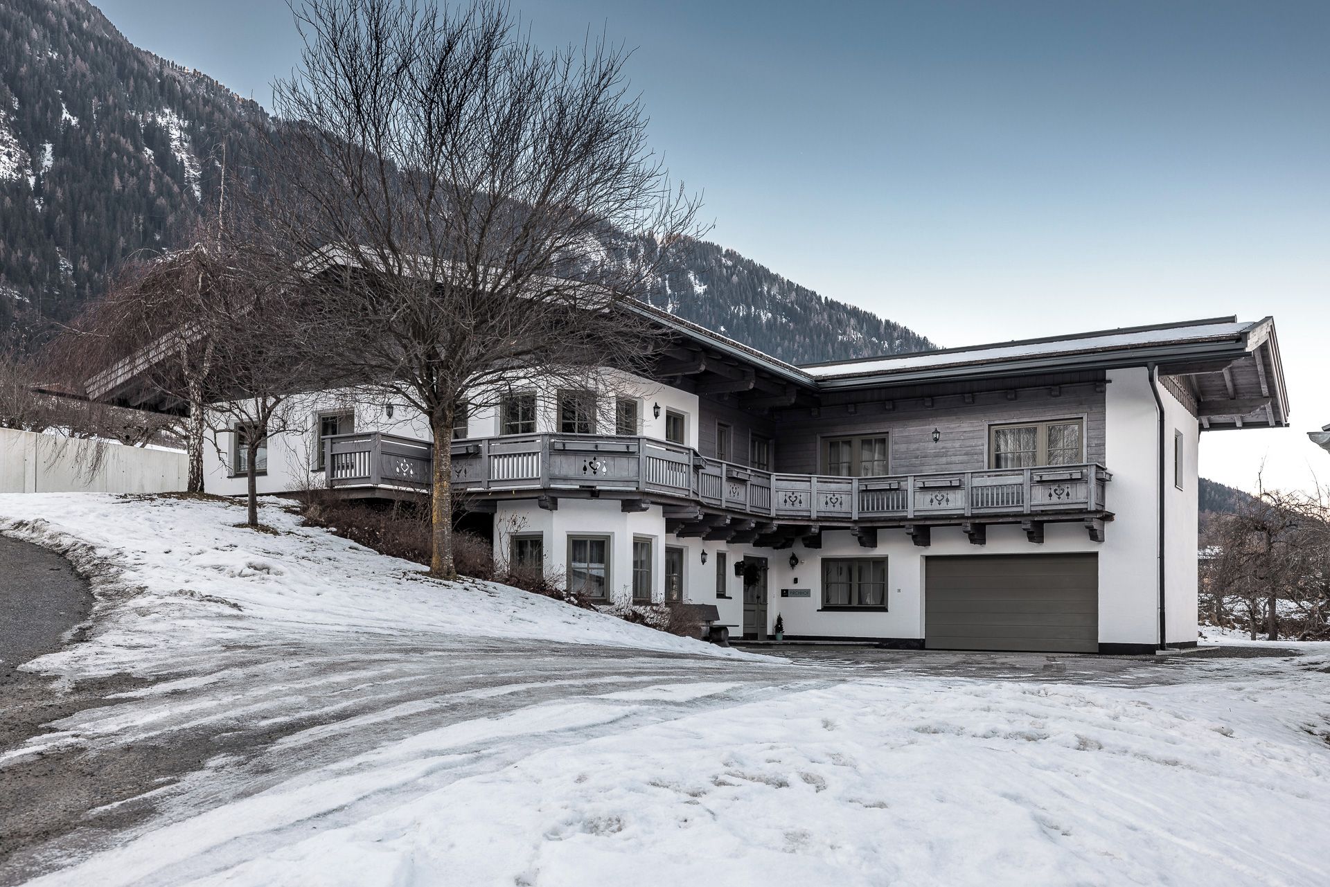 Un edificio de dos pisos con un balcón, un garaje y un paisaje cubierto de nieve.