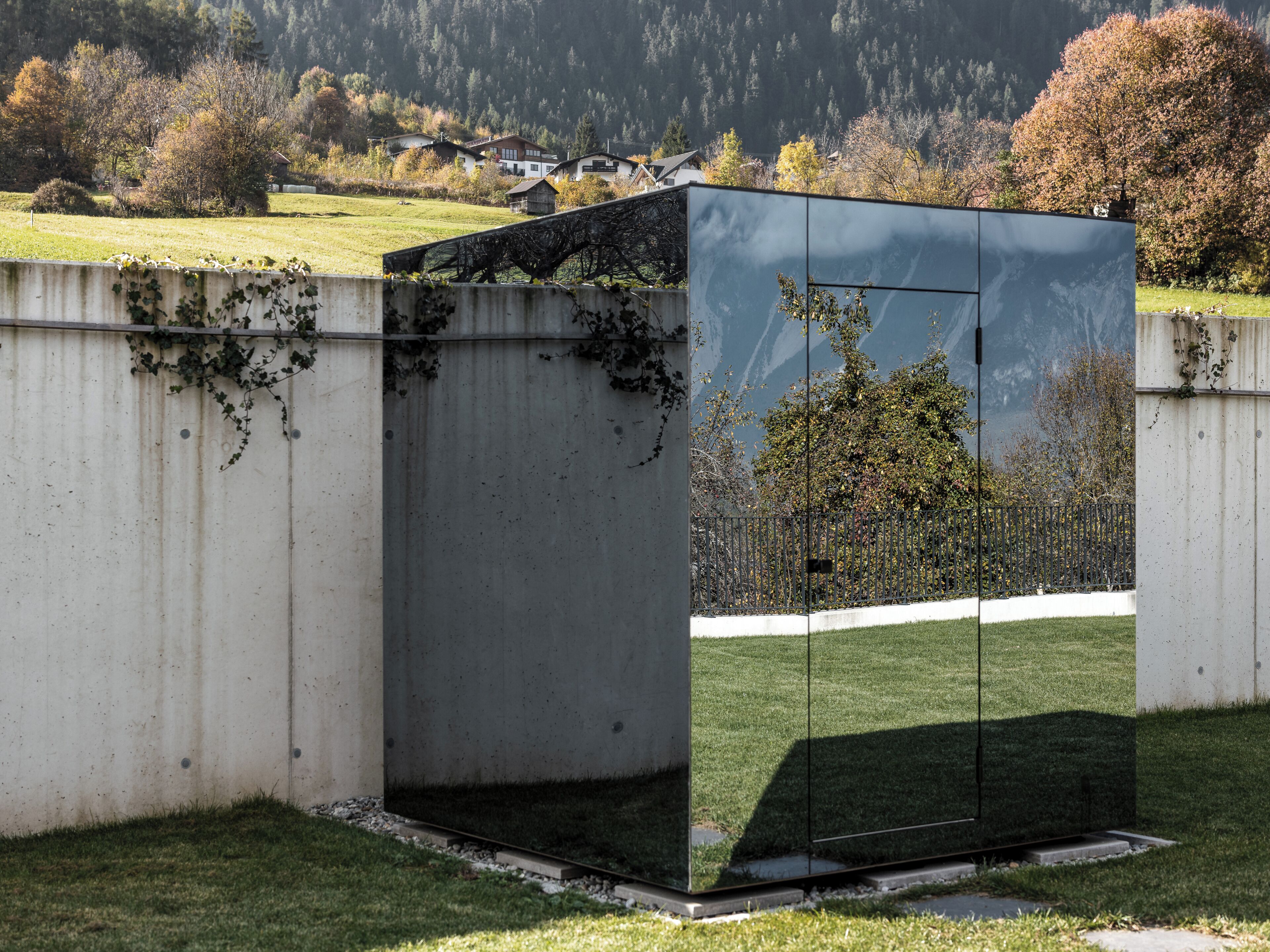 A modern building with a reflective glass facade, situated in a grassy area with a backdrop of trees and a distant mountain range.