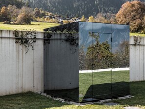 A modern building with a reflective glass facade, situated in a grassy area with a backdrop of trees and a distant mountain range. - Chalet Pirchhof by MYALPS  (Sautens)