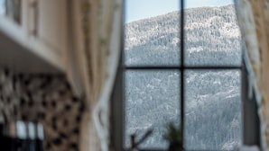 A room with a large window offering a view of a forested mountain. - Chalet Pirchhof by MYALPS  (Sautens)