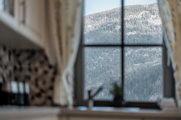A room with a large window offering a view of a forested mountain. - Chalet Pirchhof by MYALPS  (Sautens)