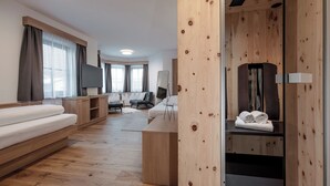 A modern hotel room with a wooden floor, a sofa, a TV, a mirror, and a wooden wardrobe. - Chalet Pirchhof by MYALPS  (Sautens)