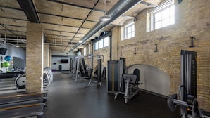 A gym with various exercise equipment, a brick wall, and large windows.