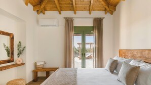 A bedroom with a wooden ceiling, a bed with multiple pillows, a bedside table with a basket, a mirror, and a window with curtains.