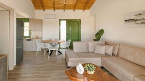 A modern living room with a wooden ceiling, a beige sofa, a dining table with white chairs, and a green door in the background.