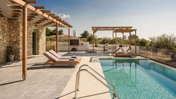 A rooftop pool area with lounge chairs, a pergola, and a stone wall.