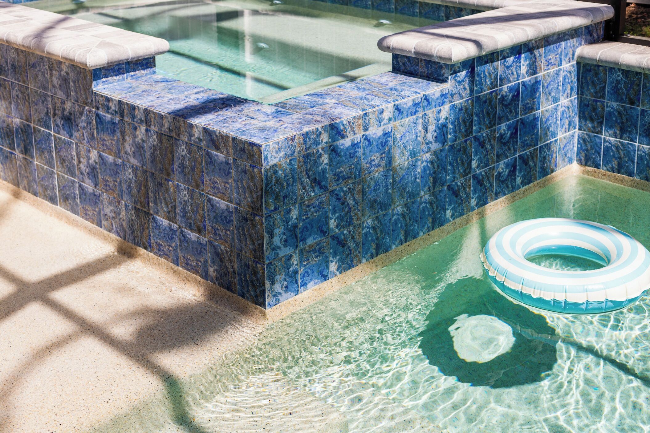 A swimming pool with blue and white tiles, a floating ring, and a stone ledge.