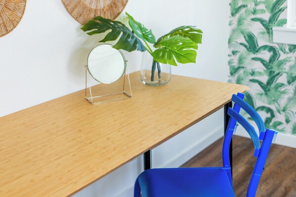 Une table en bois, surmontée d’un miroir rond et agrémentée d’un pot contenant une plante monstera.