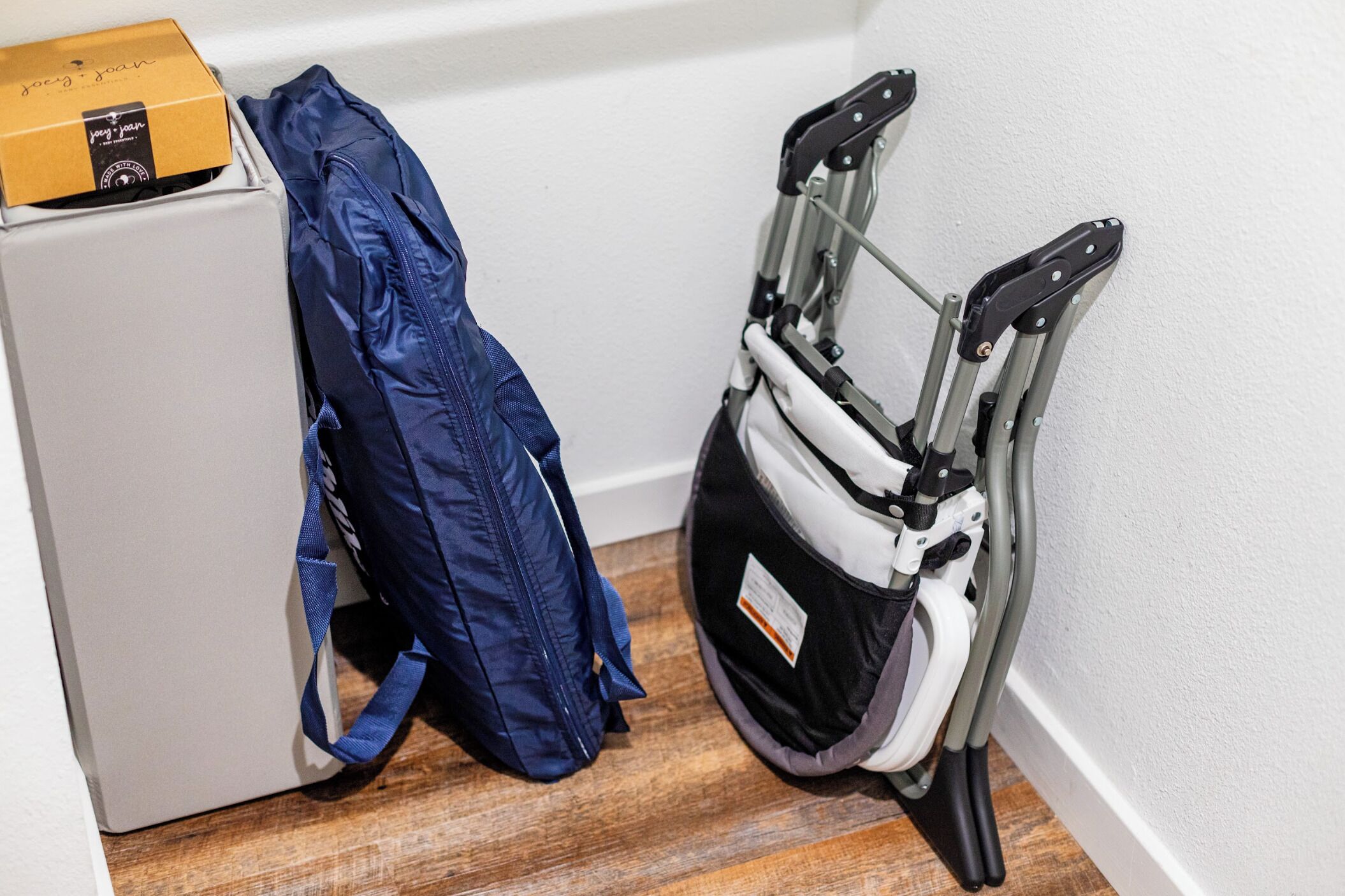 A suitcase, a blue jacket, and a wheelchair in a corner of a room.