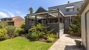 A modern house with a covered outdoor area, a well-maintained garden, and a neighboring building. - Nordic Fairway - Pet Friendly - 10 mins to Hyams Beach (Sanctuary Point)