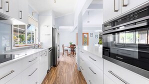 A modern kitchen with white cabinetry, stainless steel appliances, and a wooden floor. - Nordic Fairway - Pet Friendly - 10 mins to Hyams Beach (Sanctuary Point)