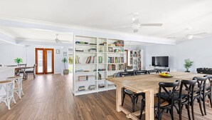 A spacious living area with a wooden dining table, black chairs, a bookshelf filled with books, a flat-screen TV, and a foosball table. - Nordic Fairway - Pet Friendly - 10 mins to Hyams Beach (Sanctuary Point)