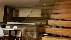 Un intérieur moderne avec un escalier en bois, un coin repas avec des chaises blanches et une cuisine en arrière-plan.