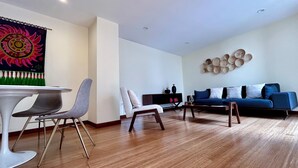 Un salon moderne avec un canapé bleu, un fauteuil blanc et un coin repas comprenant une table blanche et des chaises grises.