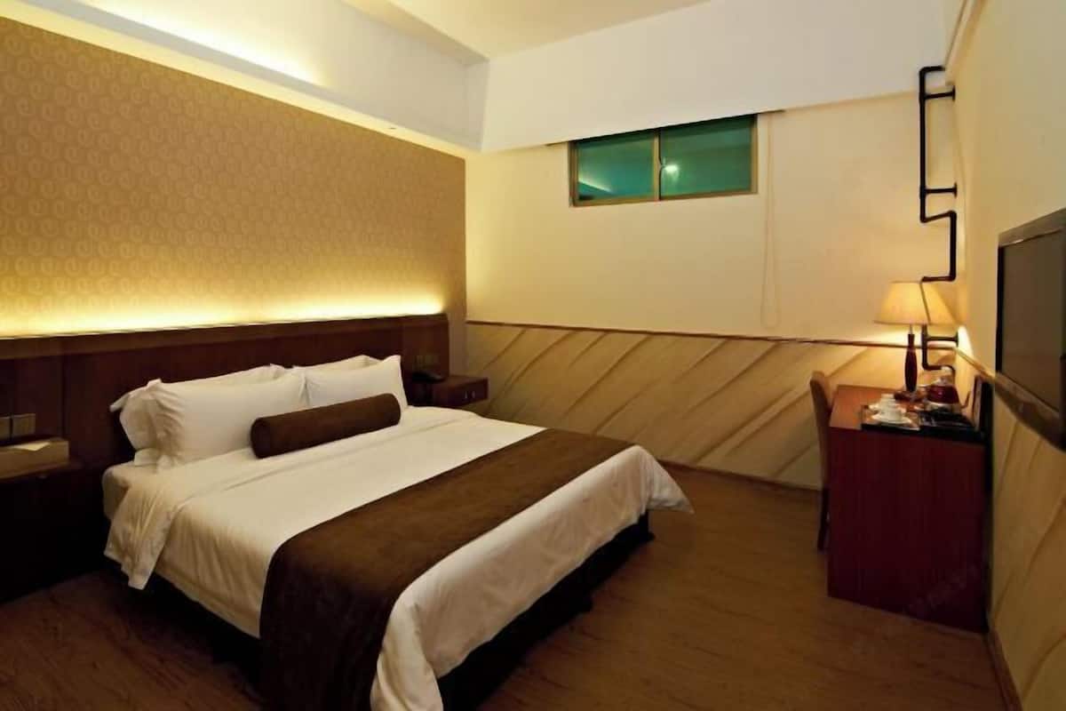 Una habitación de hotel con cama, mesitas de noche, escritorio, lámpara y televisión.