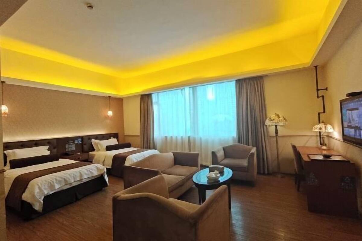 Una habitación de hotel con dos camas, un sofá, una mesita, un televisor y una lámpara.