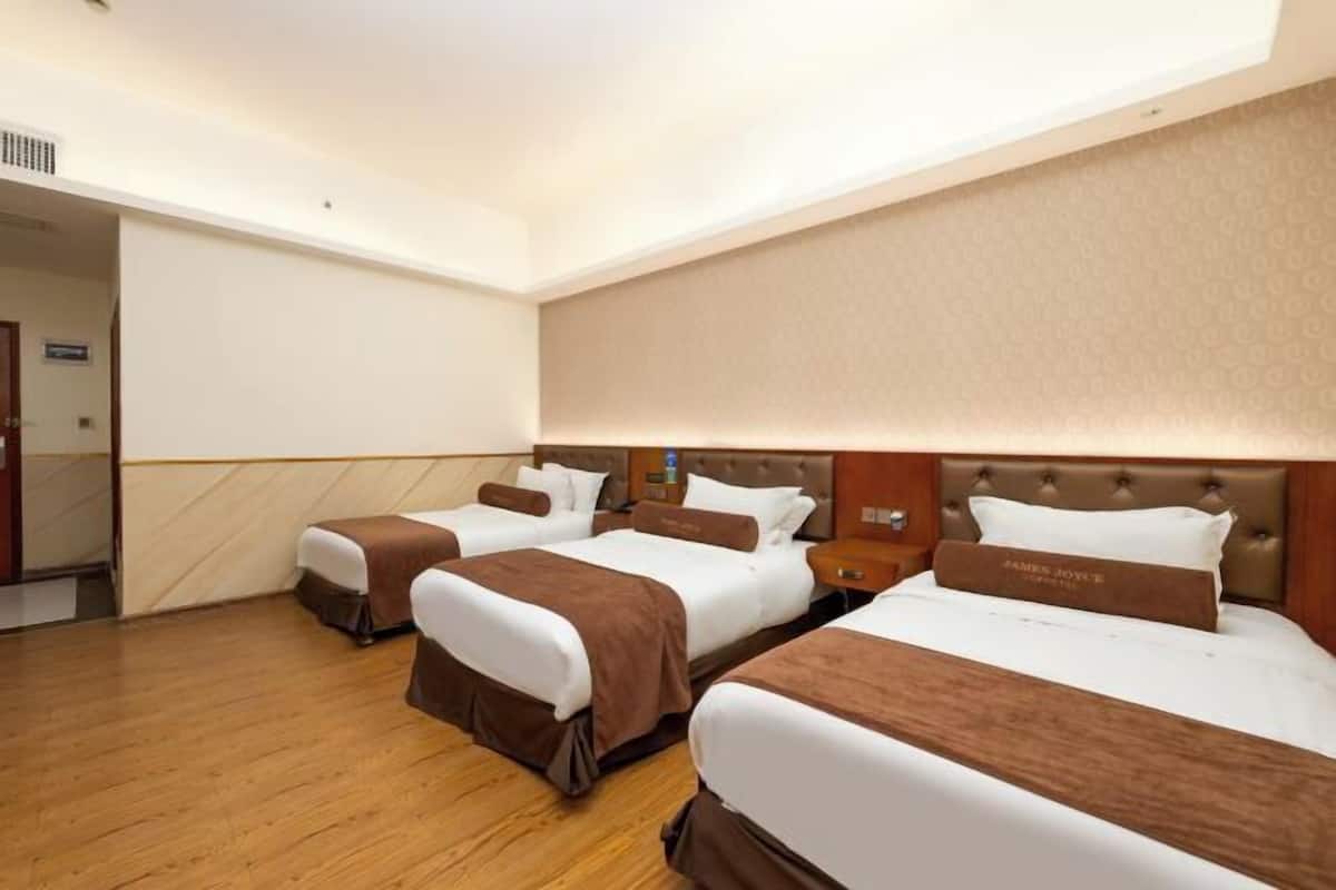 Habitación de hotel con tres camas, piso de madera y un espejo grande.