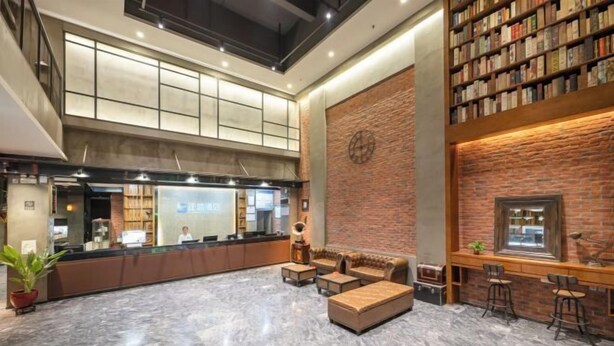 A spacious lobby with a reception desk, seating area, and a brick wall with a circular design. - Zhengsheng Hotel (Guangzhou Baiyun Railway Station Xiaoping Subway Station) (Guangzhou)