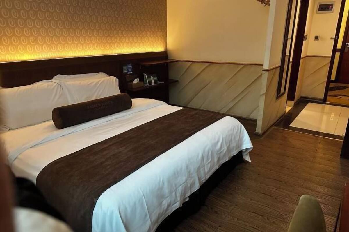 Habitación de hotel con una cama grande, cabecera de madera, mesita de noche con lámpara y pared con estampado.