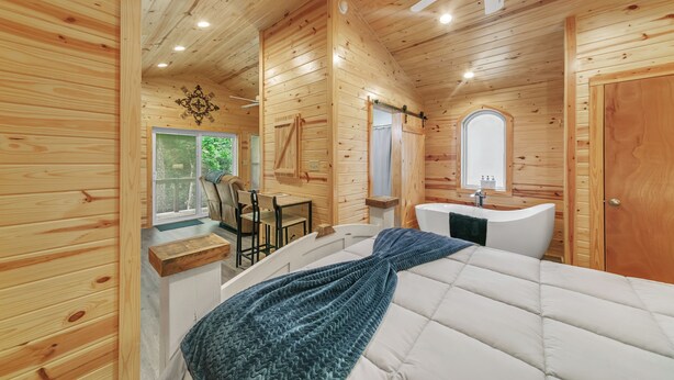 A wooden cabin interior with a bed, a bathroom, and a dining area.