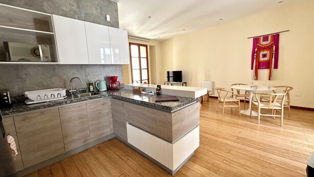 A modern kitchen with a granite countertop, white cabinets, and a built-in oven. There is a dining area with a round table and chairs, and a TV mounted on the wall. - La Ronda 431 - Apt. #104 (Quito)