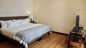 A hotel room with a large bed, a bedside table with a lamp, a TV, and a wooden floor. - La Ronda 431 - Apt. #103 (Quito)