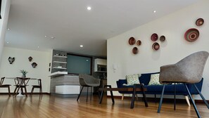 A modern living room with a blue sofa, two armchairs, and a coffee table. There are decorative woven baskets on the wall and a staircase leading to the kitchen. - La Ronda 431 - Apt. #103 (Quito)