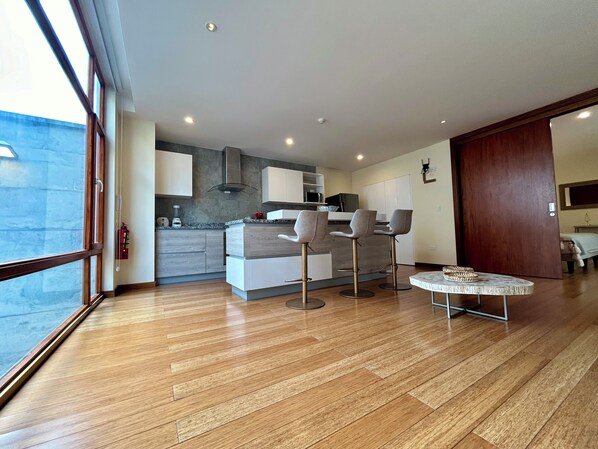 A modern kitchen with wooden cabinets, a built-in oven, and a dining area with two bar stools and a round table.