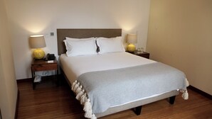 Ein ordentlich bezogenes Bett mit weißen Leinen, einer grauen Tagesdecke und zwei Nachttischlampen.