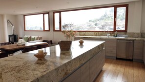 Une cuisine moderne dotée d’un grand îlot central, d’un coin repas avec une table et des chaises, et offrant une vue sur une colline grâce à de grandes fenêtres.