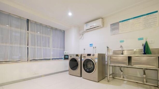 A laundry room with two front-loading washing machines, a sink with a stainless steel countertop, and a large window with sheer curtains. - City Comfort Inn(Wuhan Jiangxia Branch) (Wuhan)
