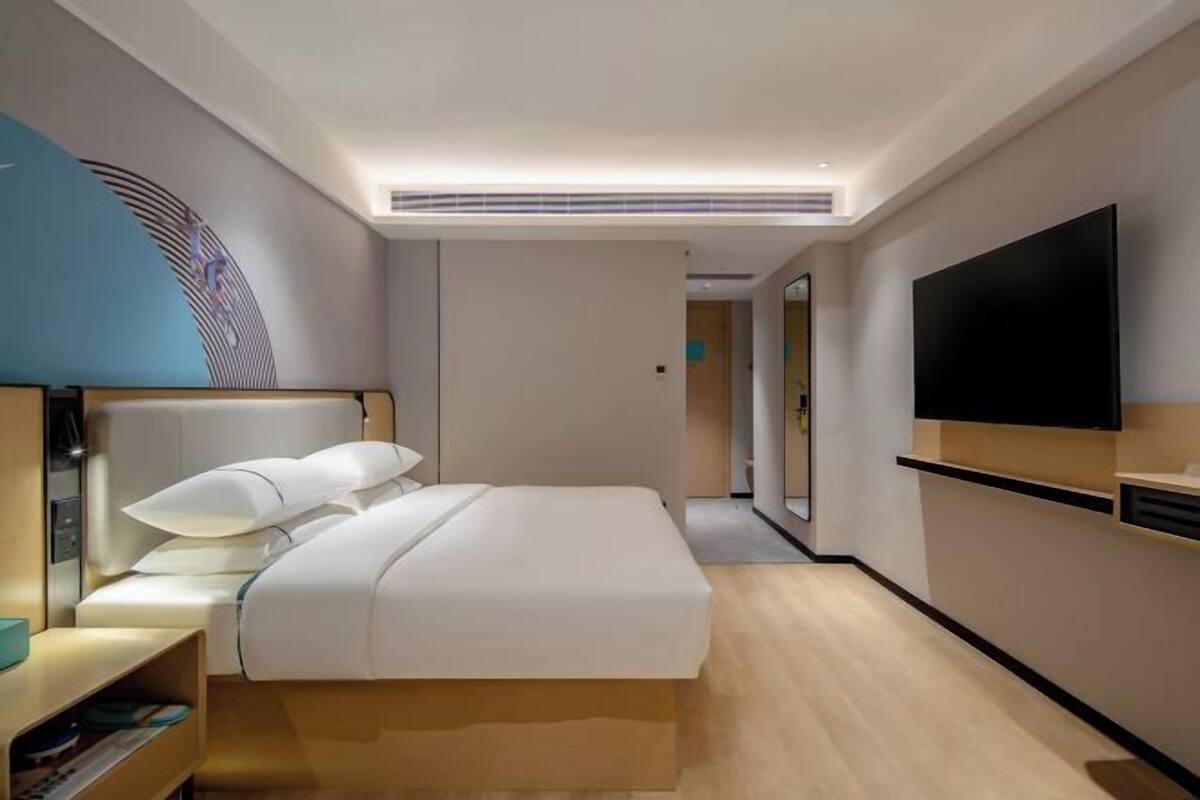 A modern hotel room with a large bed, a flat-screen TV, a bedside table, and a wall-mounted TV.