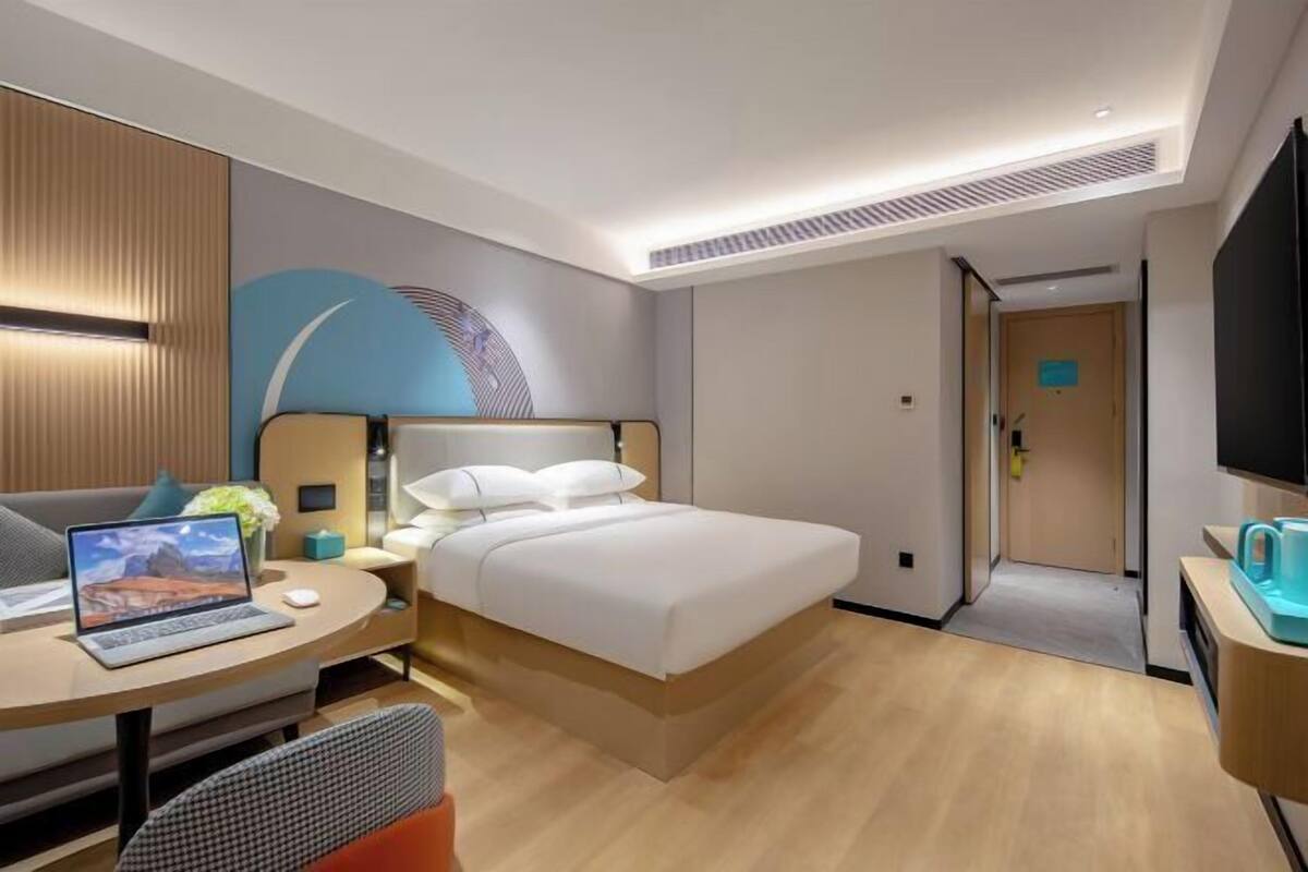 A modern hotel room with a bed, a desk with a laptop, a chair, and a TV.