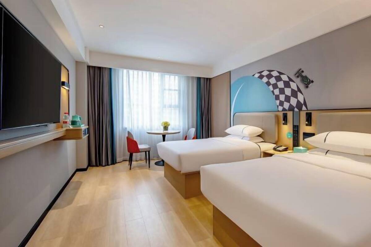 A hotel room with two beds, a desk, a chair, a TV, and a window with curtains.