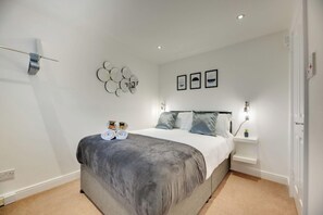 Un dormitorio moderno con una cama grande, mesitas de noche, luces fijadas a la pared y un espejo decorativo.