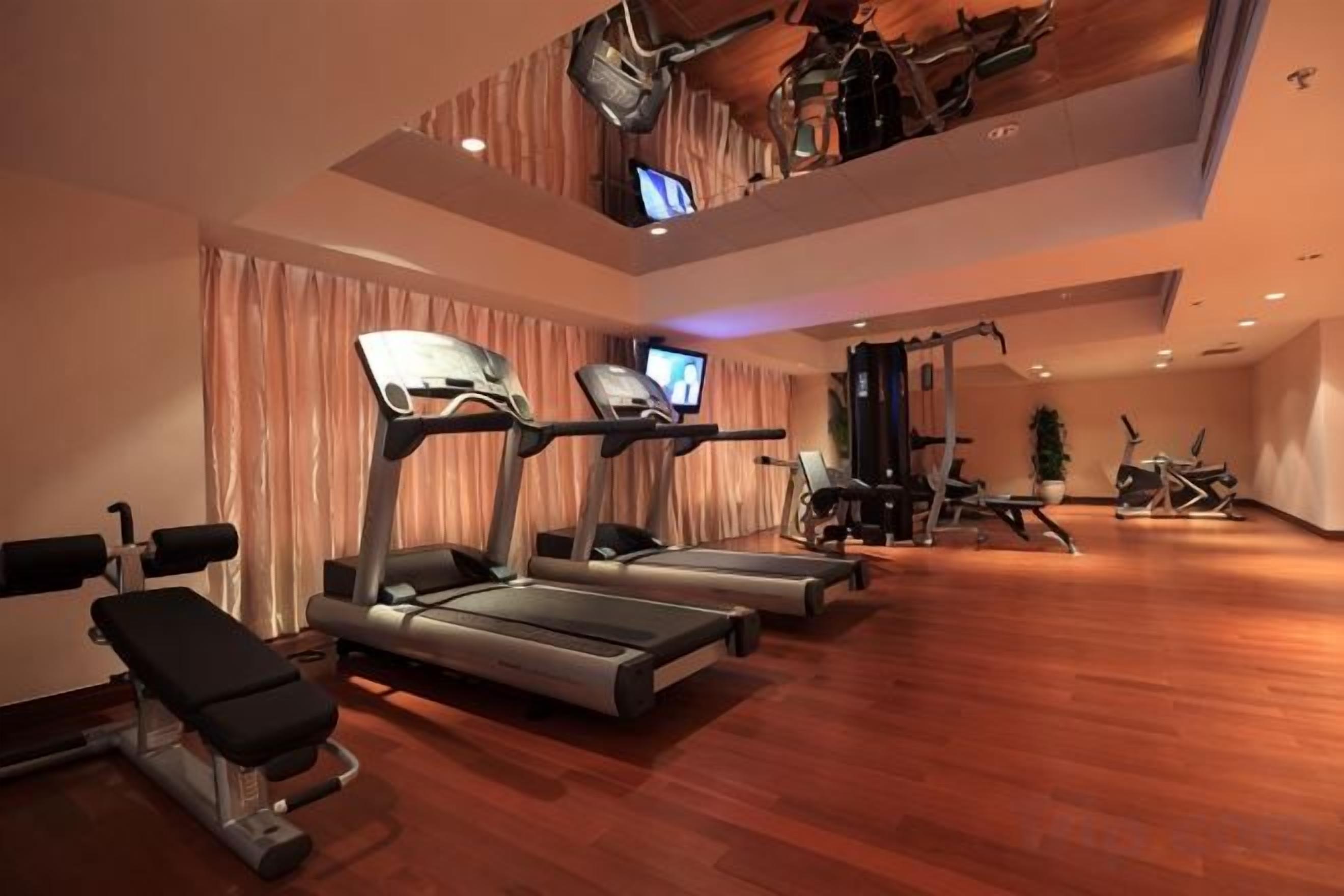 Academia com esteiras, equipamentos de ginástica e televisão.