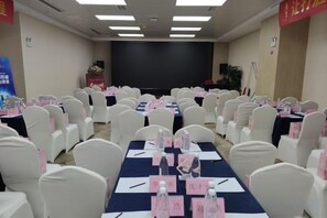 A conference room with rows of white chairs, tables with name cards, and a stage at the front.