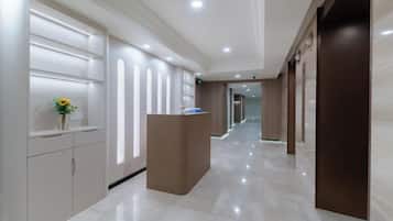 A hotel reception area with a reception desk, a vase with a flower, and a corridor leading to other rooms.
