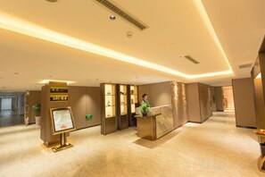 A hotel reception area with a reception desk, a digital information board, and a potted plant. - Spring Downtown Hotel (Chengdu)