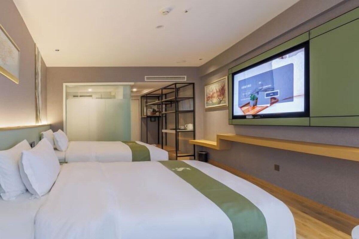 A hotel room with two beds, a television on the wall, and a small seating area with a shelf.