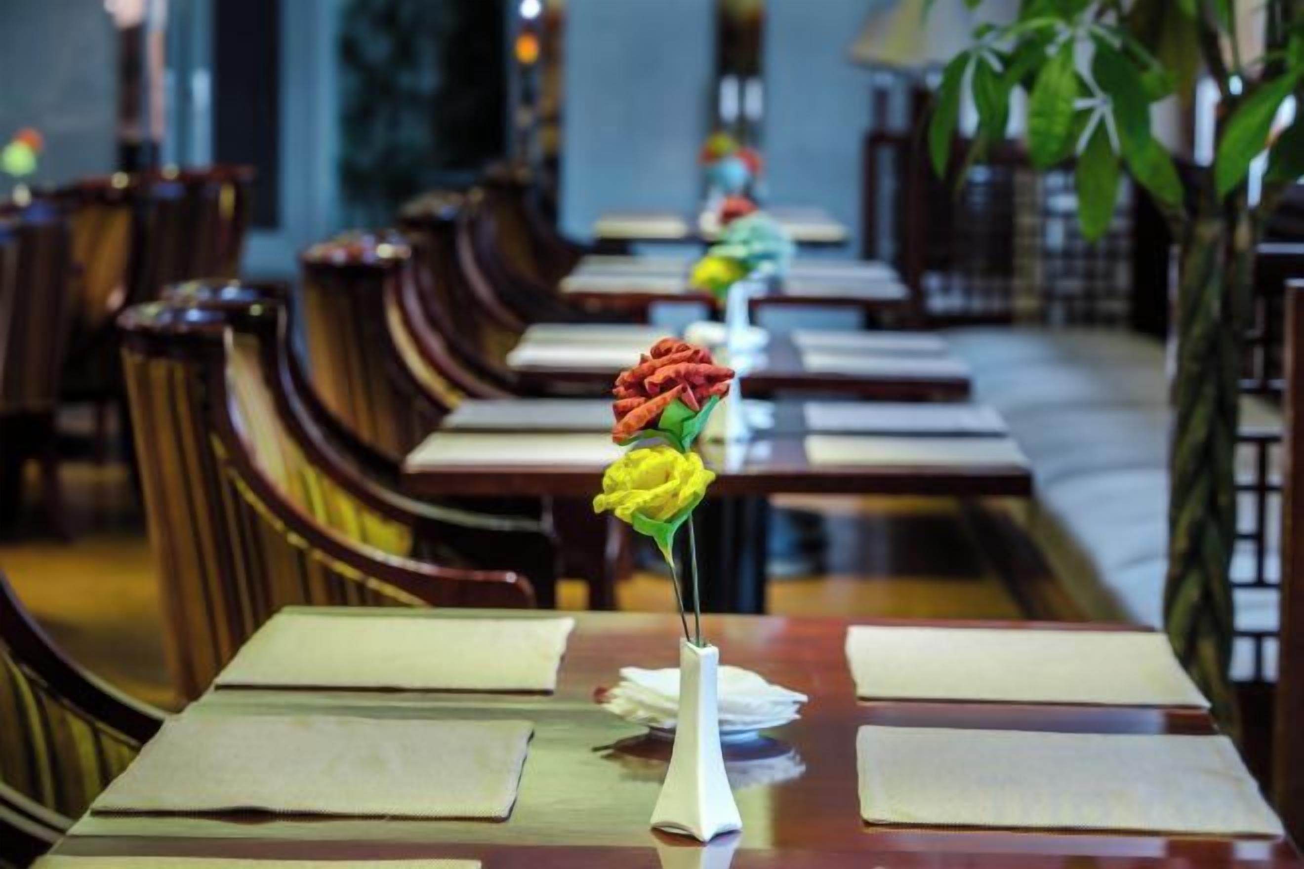 Un restaurante con mesas y sillas de madera, un jarrón con un centro de flores y una barra larga.