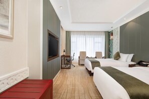 Ett hotellrum med två sängar, ett skrivbord, en TV och ett fönster med gardiner.