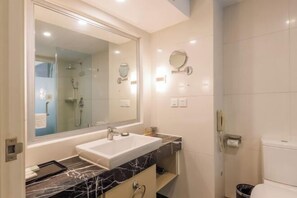 A modern bathroom with a large mirror, a white sink, a marble countertop, a glass-enclosed shower, and a toilet. - Spring Downtown Hotel (Chengdu)