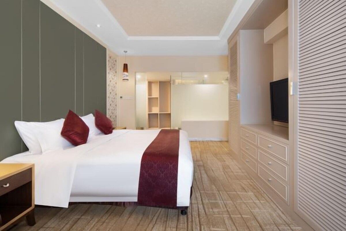 A modern hotel room with a large bed, bedside tables, a TV, and a walk-in closet.