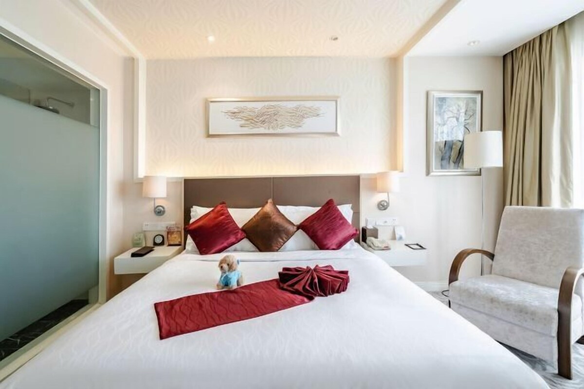 A hotel room with a large bed, a headboard, a nightstand, a chair, and a wall-mounted lamp.