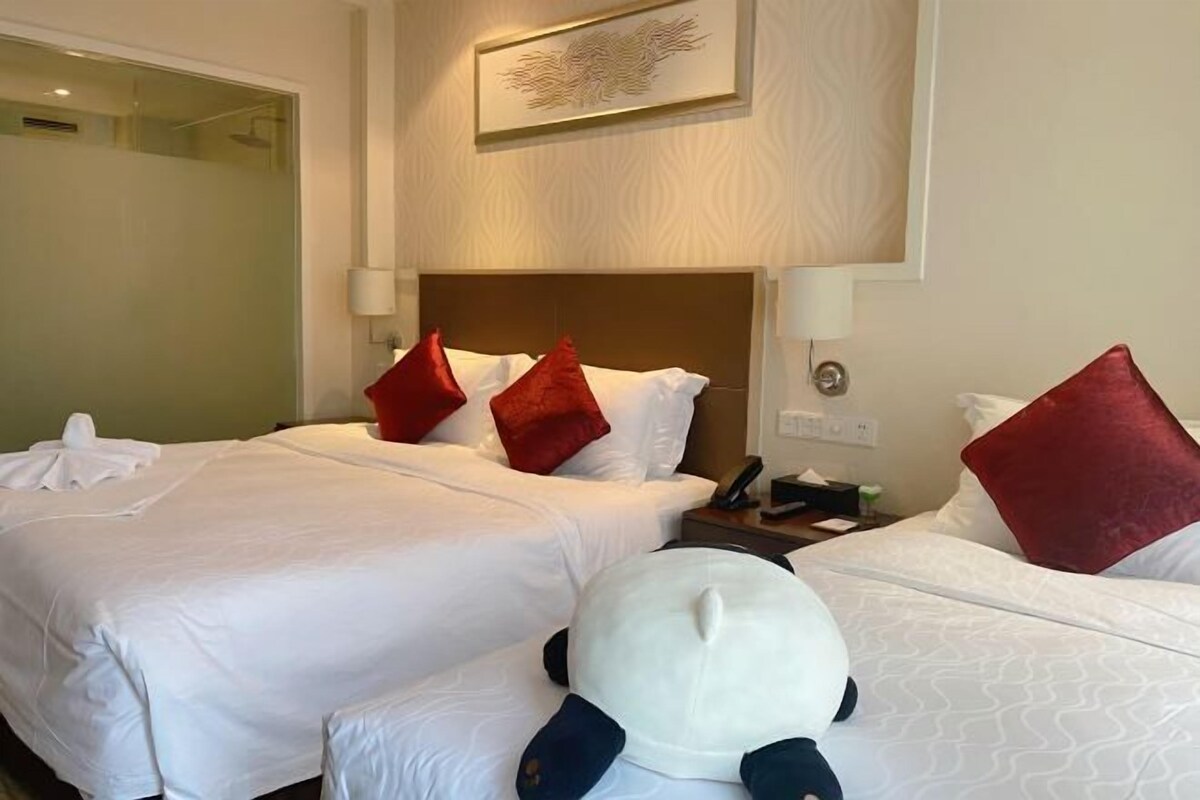 A hotel room with two beds, each with white linens and red pillows. There is a nightstand with a phone and a lamp.