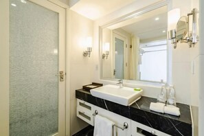 A modern bathroom with a large mirror, a white sink, black marble countertop, and a glass shower enclosure. - Spring Downtown Hotel (Chengdu)