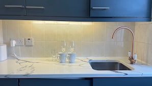 A kitchen with dark cabinets, a white countertop, a sink with a copper faucet, and two glasses on the counter. - Baker Street Apartments (London)